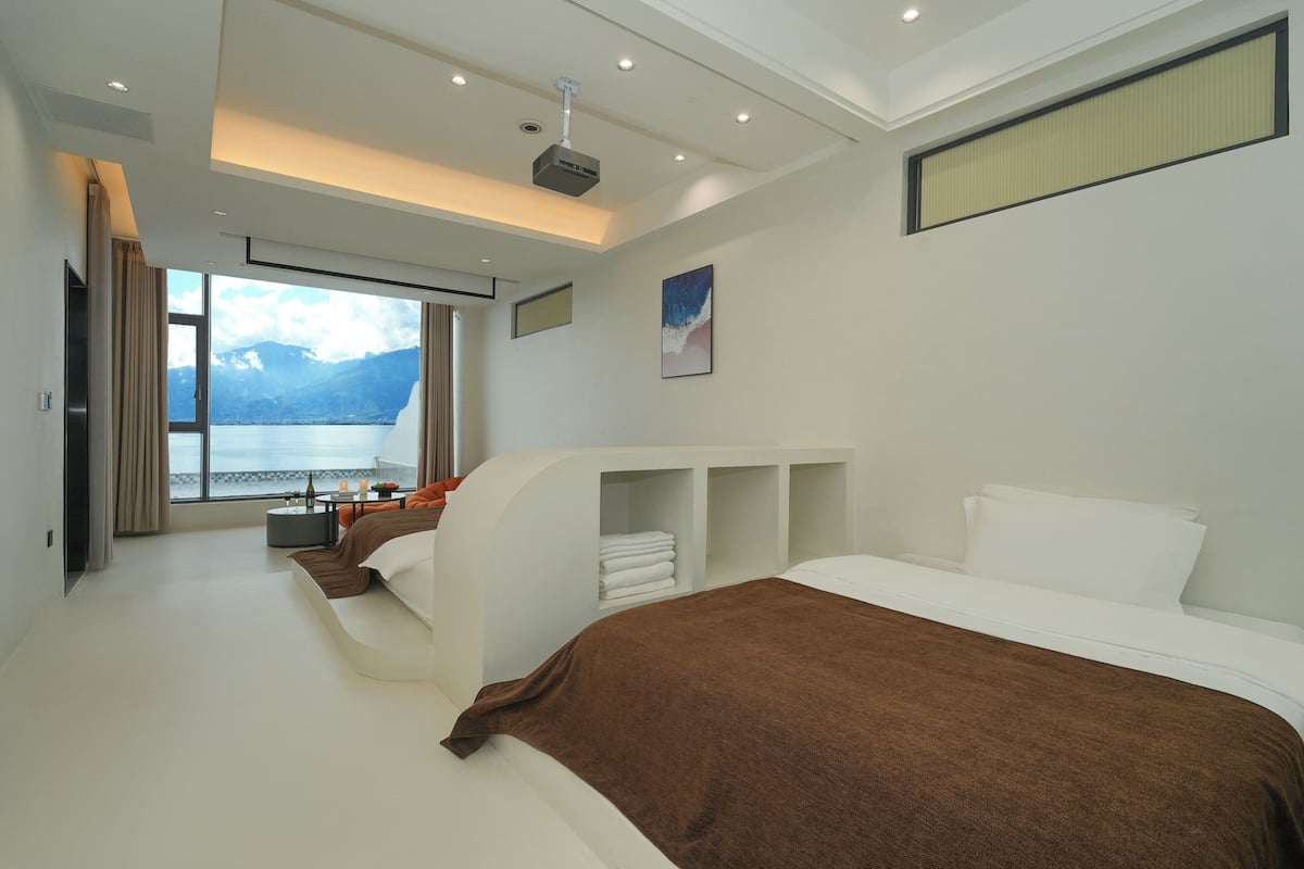 Una habitación de hotel moderna con una cama grande, un área de descanso con vista al lago y un proyector en el techo.