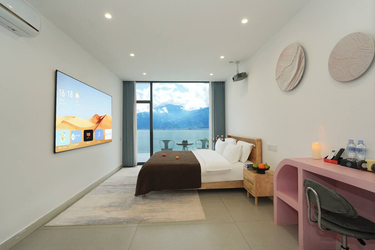 Habitación de hotel moderna con cama, escritorio, silla, televisión y vistas a las montañas.