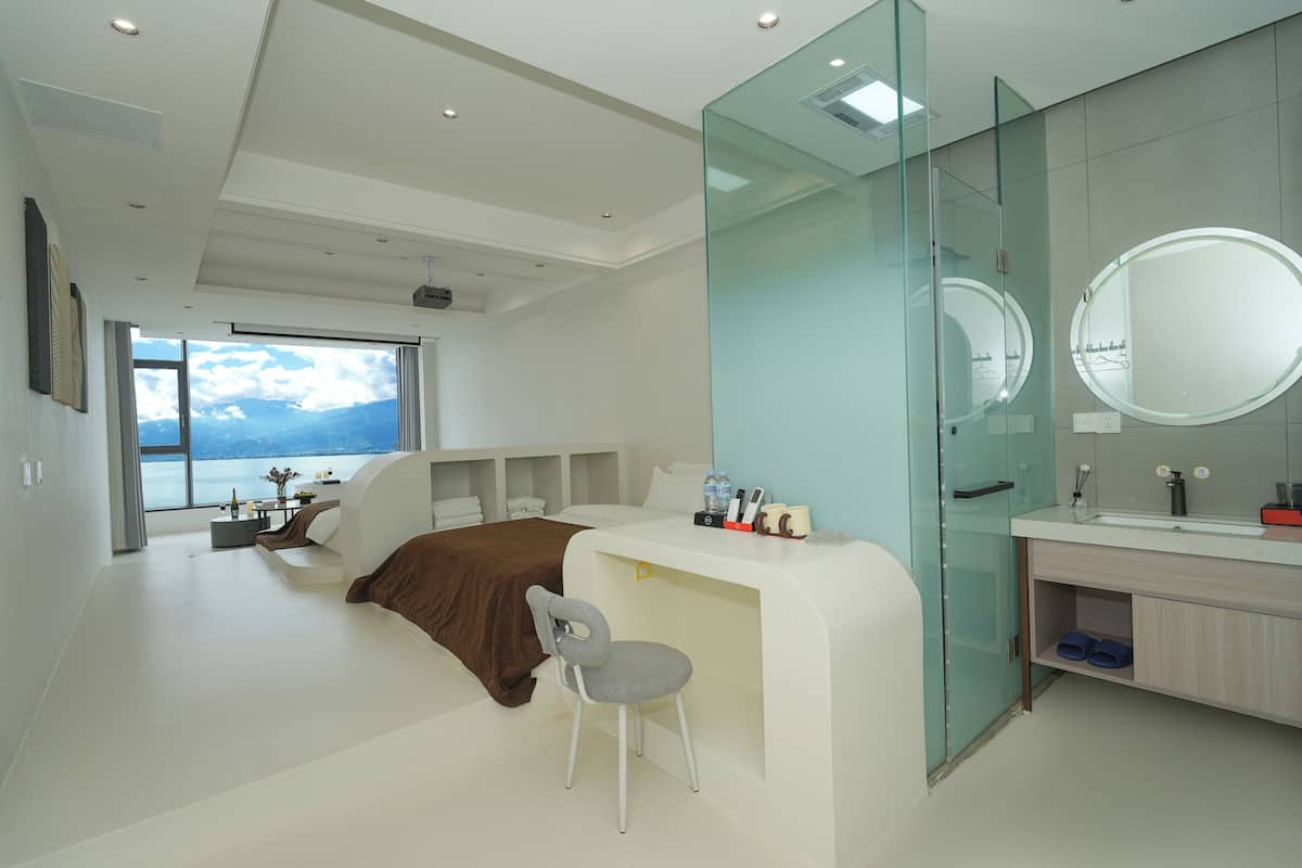 Un dormitorio moderno con una cama grande, un escritorio, una silla, un tocador con espejo y vistas al exterior.