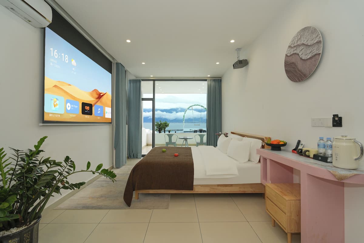 Habitación de hotel moderna con cama, mesita de noche y una pantalla grande que muestra la hora y el clima.