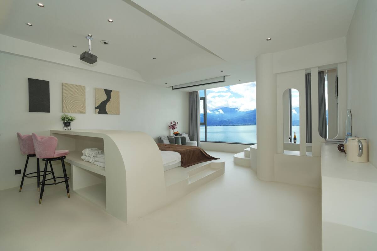 Un dormitorio moderno con cama, escritorio y silla. Se ve una ventana con vistas a montañas.