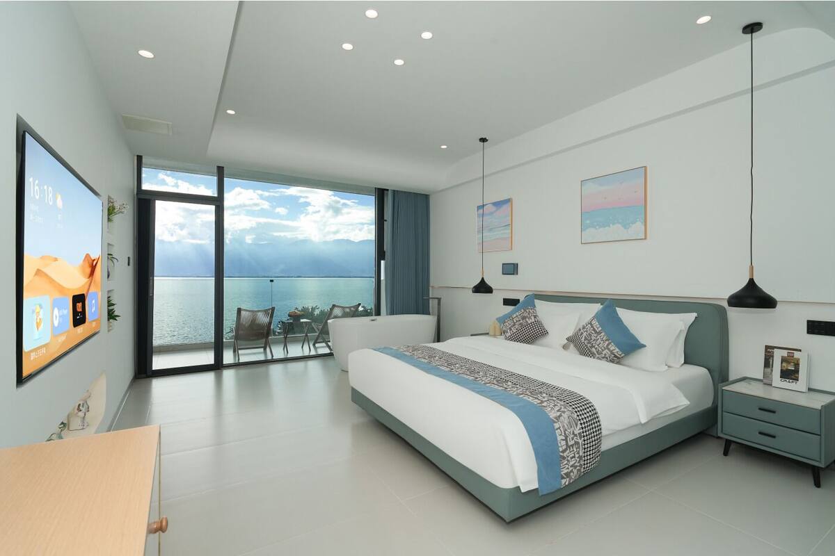 Un dormitorio moderno con una cama grande, vistas al mar y un balcón con mobiliario exterior.