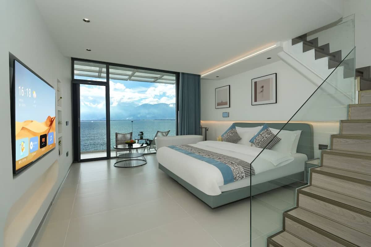 Un dormitorio moderno con una cama grande, una escalera de cristal y vista al mar.