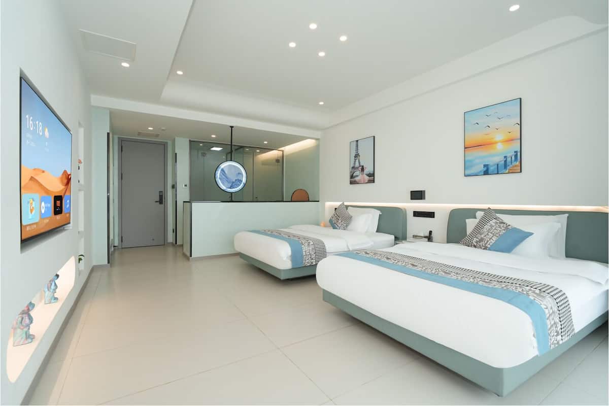 Habitación de hotel moderna con dos camas, un espejo grande, obras de arte en las paredes y un televisor de pantalla plana mostrando la hora.