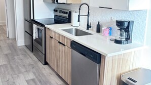 Moderni keittiö, jossa on valkoiset kaapit, ruostumattomasta teräksestä valmistettu jääkaappi, mikroaaltouuni, astianpesukone ja kahvinkeitin.