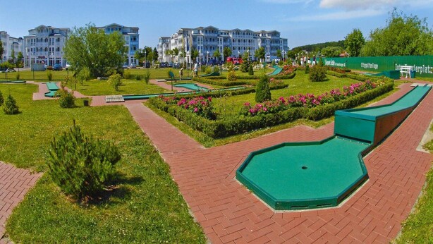 A golf course with a putting green, a brick pathway, and a large building in the background. - Ferienwohnungen im Seepark Sellin (Sellin)