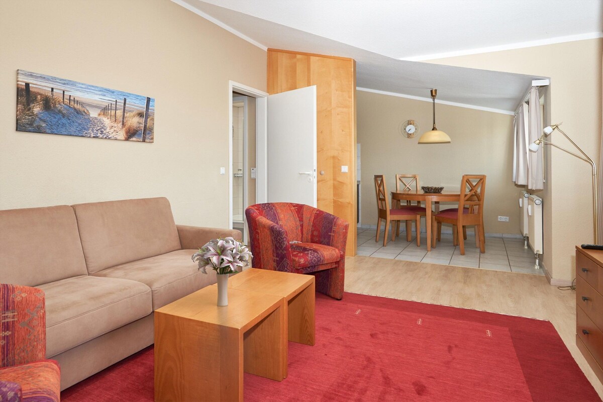 A living room with a sofa, armchair, coffee table, and a dining area with a table and chairs.