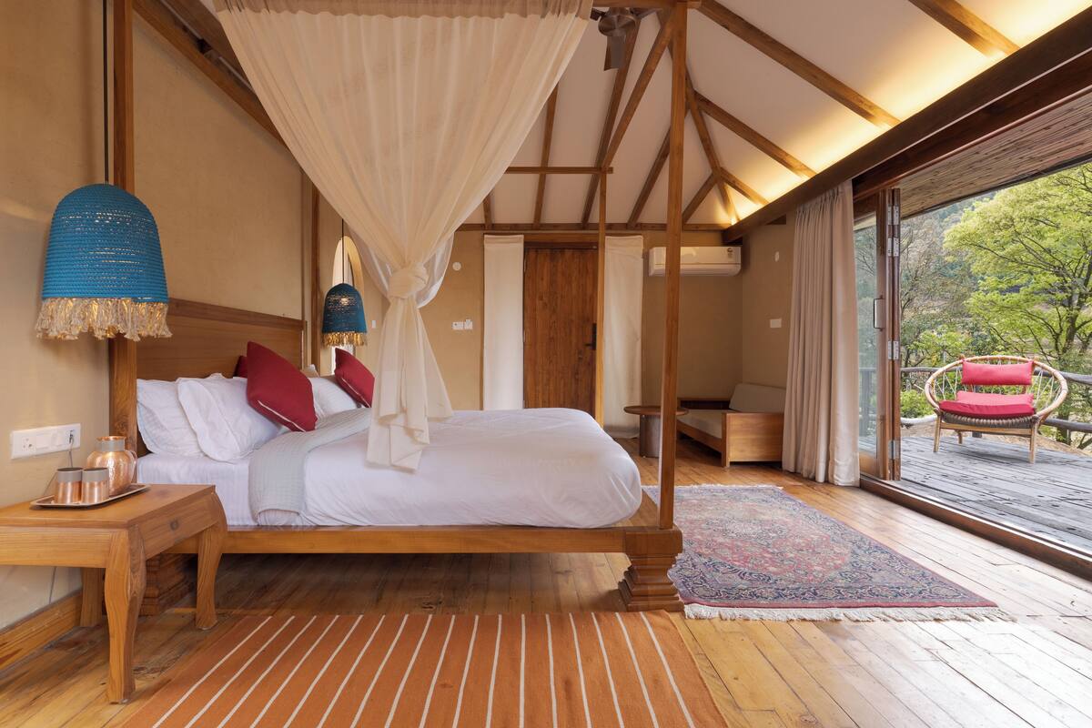 Un dormitorio con cama con dosel, suelo de madera, una mesita de noche con lámpara y vistas al exterior.