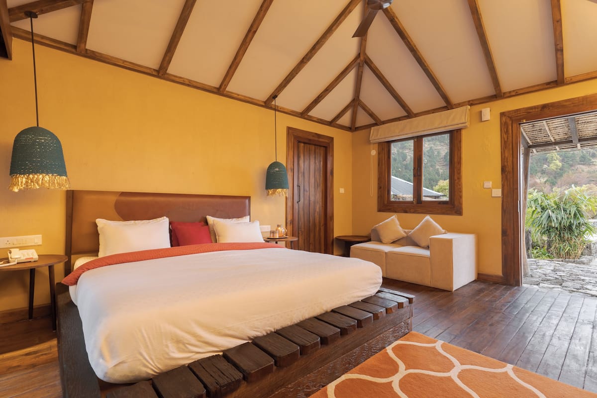 Un dormitorio con una cama grande, cabecera de madera, dos mesitas de noche, un sofá y vistas al exterior.