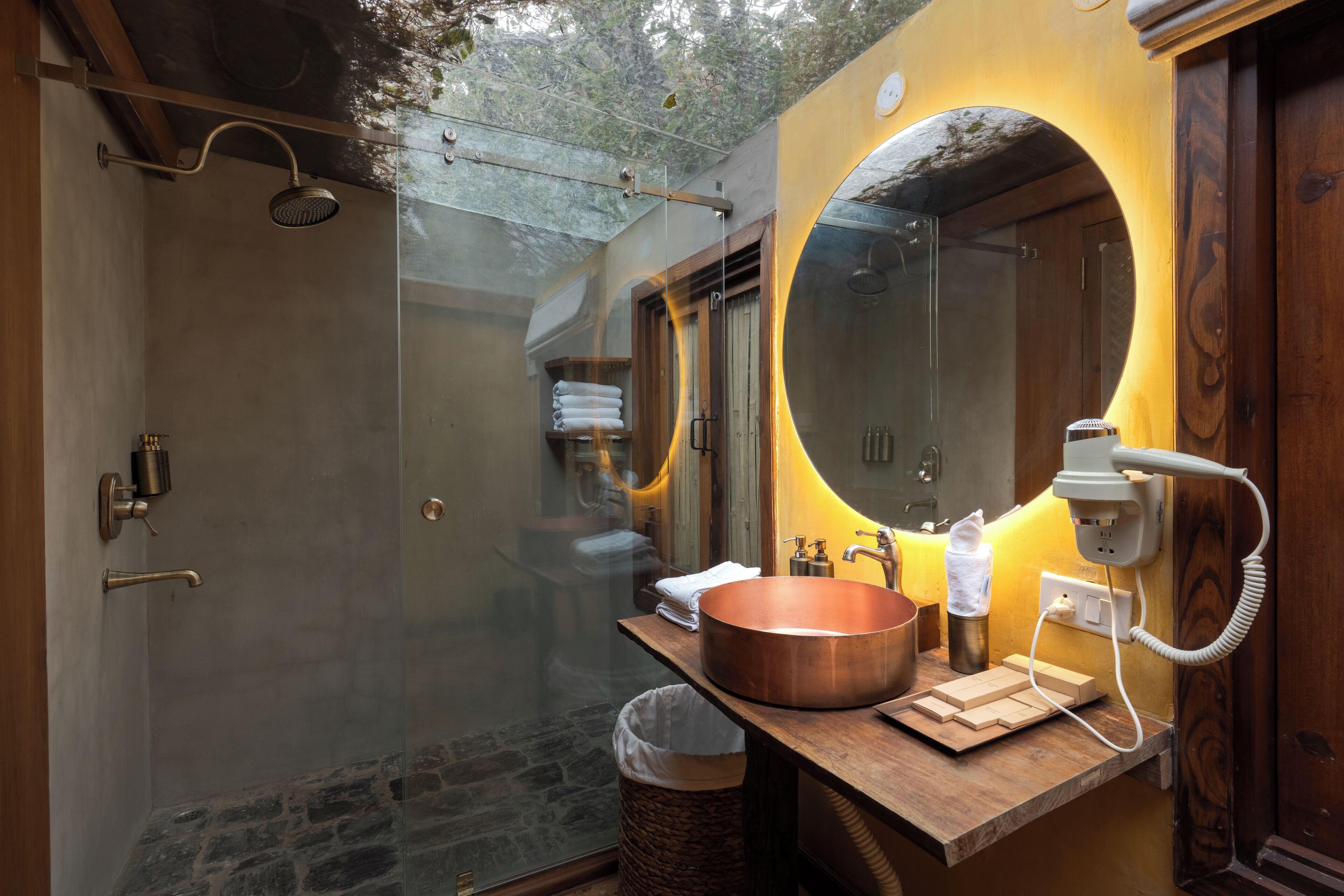 A modern bathroom with a glass-enclosed shower, a copper sink, and a wooden vanity.