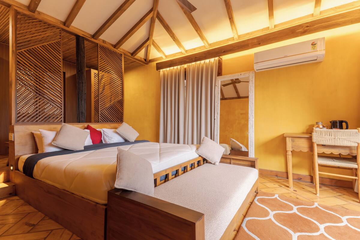 Un dormitorio con una cama, cabecera de madera, cortinas, un espejo y una mesita de noche con lámpara.