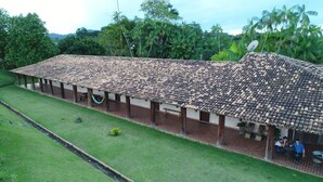 A long, covered outdoor area with a tiled roof, benches, and a grassy lawn. - Muiraquitã Hotel  (Ourilandia Do Norte)