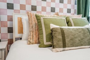 Un lit bien fait, recouvert d’une couette blanche et agrémenté de plusieurs coussins décoratifs aux motifs et couleurs variés.