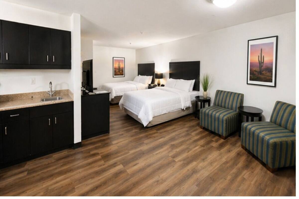A hotel room with a kitchenette, two beds, a seating area, and a desert-themed wall art.