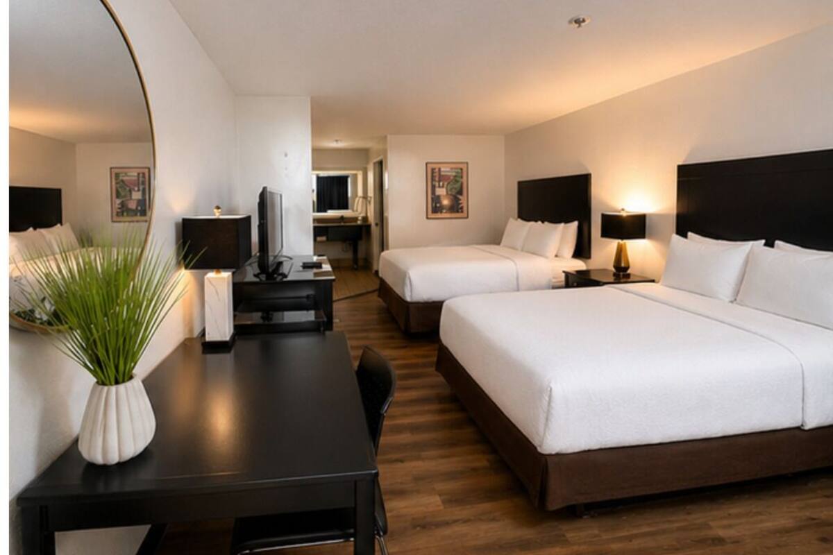 A hotel room with two beds, a desk, a chair, a TV, and a large mirror.