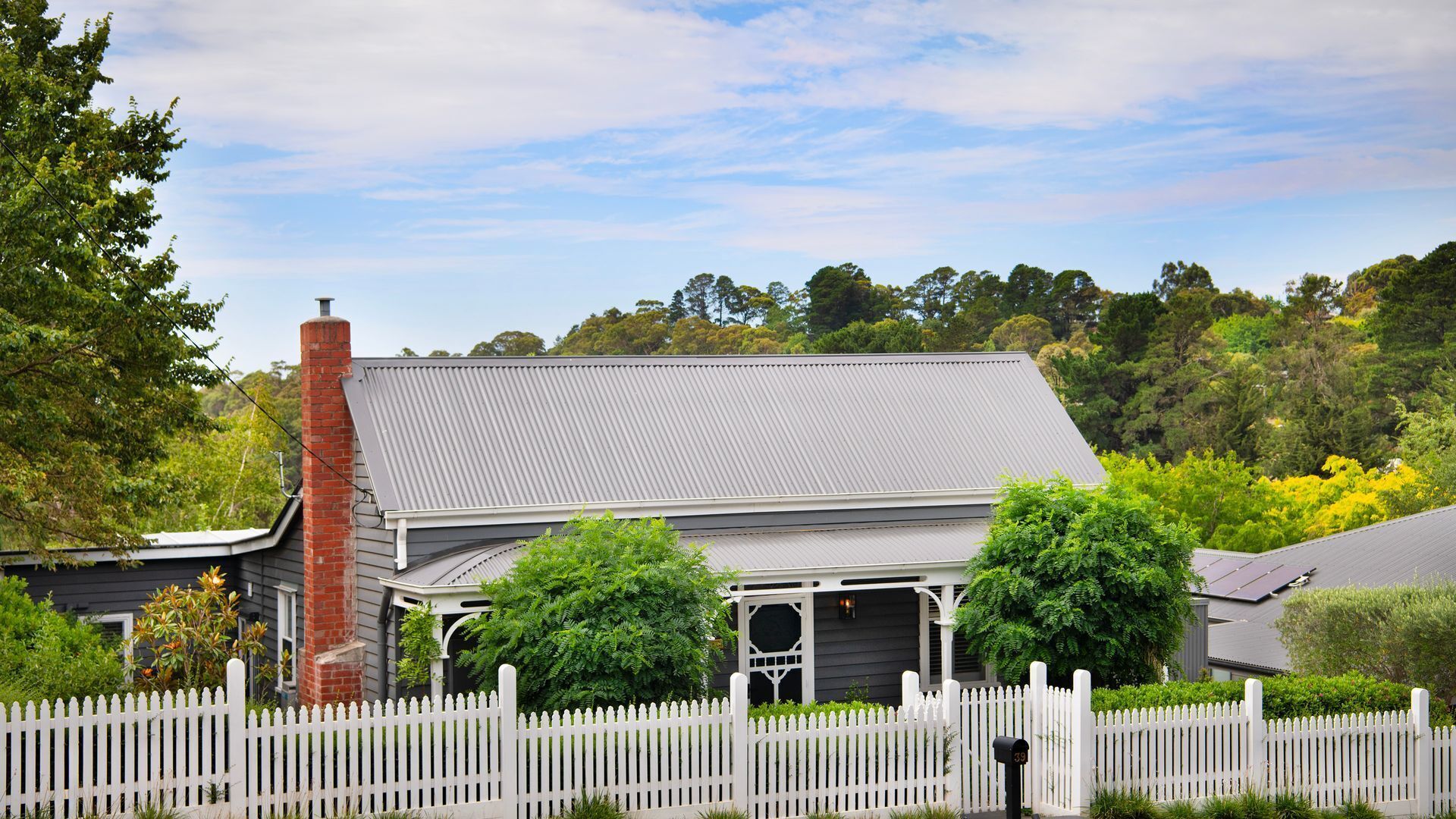 A house with a grey roof, white picket fence, and surrounded by greenery.