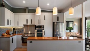 A modern kitchen with white cabinets, stainless steel appliances, a wooden island, pendant lighting, and a view of the outdoors. - Bengarlyn in Daylesford where bold garden design meets boutique luxury, stunning 3 bedroom home (Daylesford)