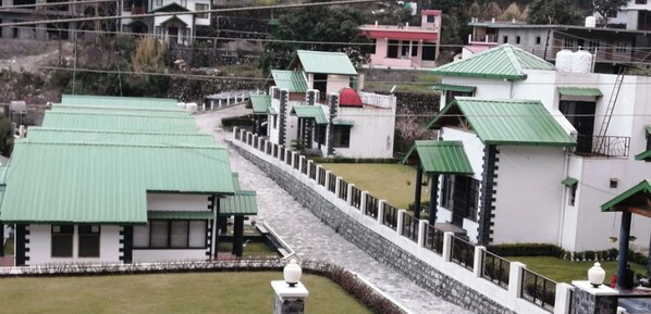 A series of buildings with green roofs and white walls, arranged in a linear fashion along a stone pathway. - Aesquire Hotel (Nainital)