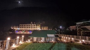 A building with multiple floors, a green roof, and a white fence with lights.