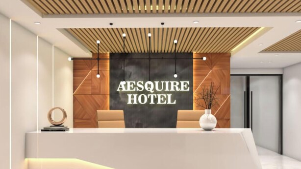 A modern hotel reception desk with a wooden panel wall and a large sign reading "Aesquire Hotel".