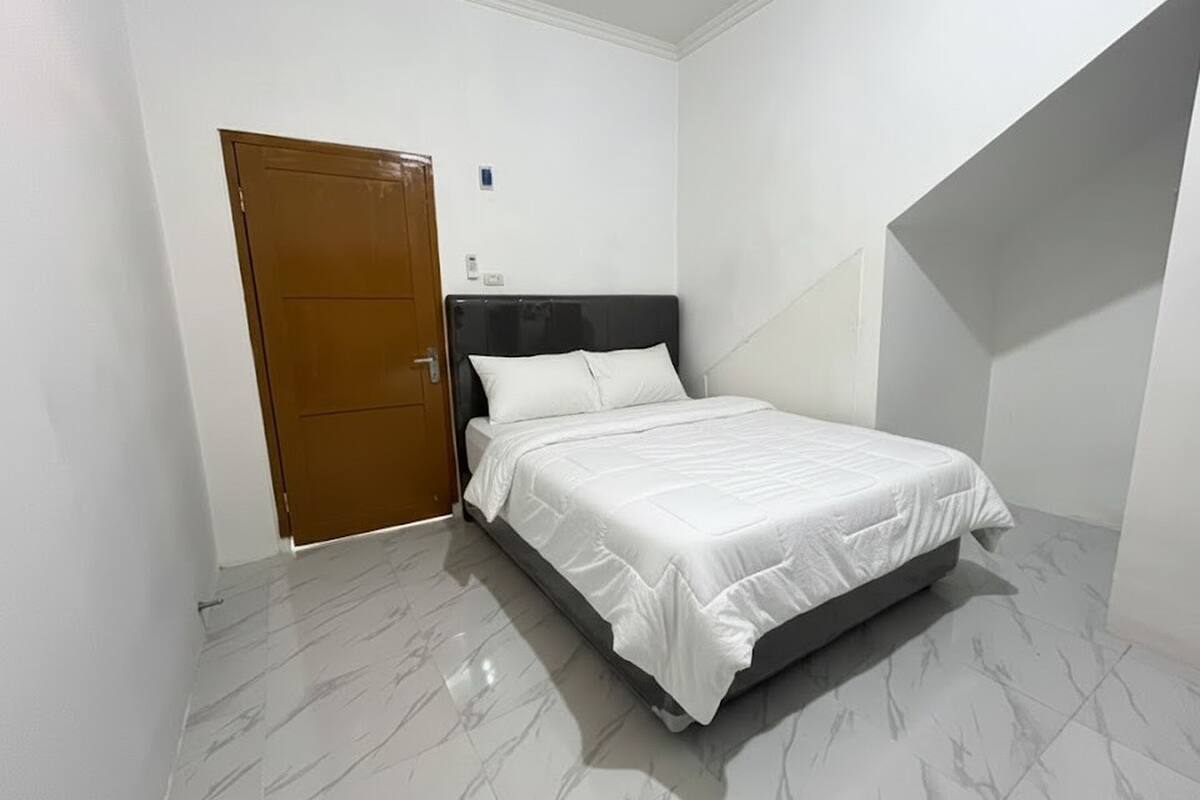 A bedroom with a bed, a wooden door, and a white wall.