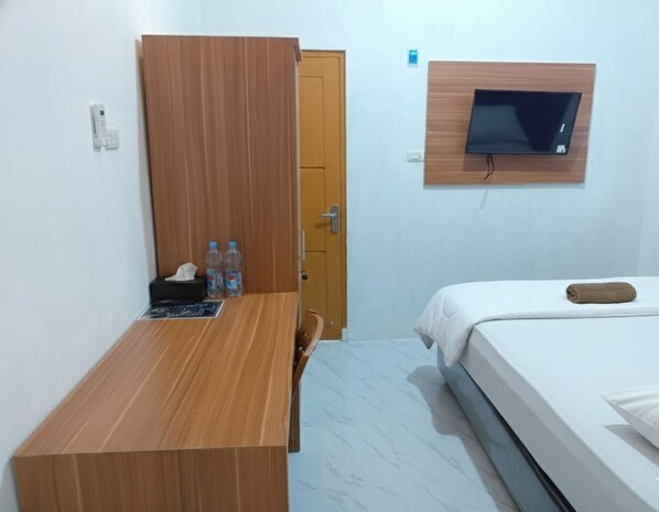 A hotel room with a wooden desk, a bed, a TV mounted on the wall, and a door leading to another room. - Collection O PH18 Bandar Lampung (Bandar Lampung)
