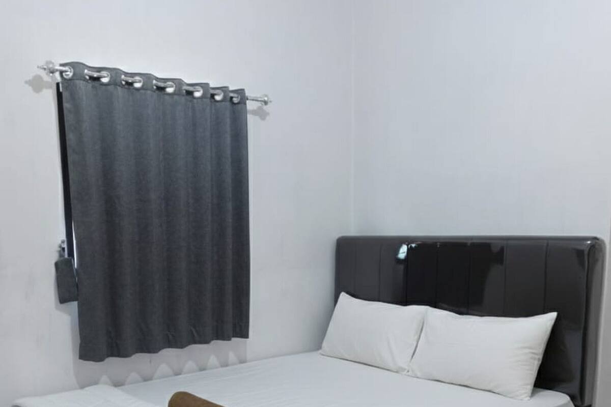 A single bed with a dark headboard, white bedding, and a brown towel.