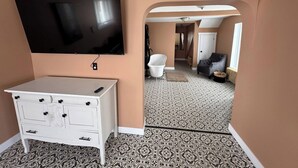A room with a flat-screen TV mounted on the wall, a white dresser with drawers, patterned floor tiles, and a doorway leading to another room. - The Red Farm Suite at The Red Farm (Howie Centre)