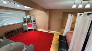 A bedroom with a red carpet, a vanity with a mirror, a bed with white curtains, and a window with blinds. - The Red Farm Suite at The Red Farm (Howie Centre)