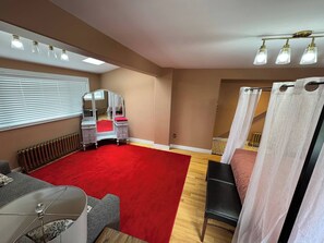 Un dormitorio con alfombra roja, un tocador con espejo, una cama con cortinas blancas y una ventana con persianas.
