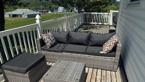 A covered outdoor seating area with a wicker sofa, two cushions, and a matching ottoman. - The Red Farm Suite at The Red Farm (Howie Centre)