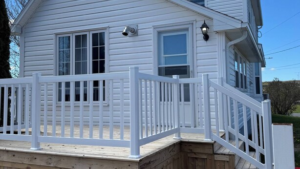 A two-story white house with a wooden deck and a white railing. - The Red Farm Suite at The Red Farm (Howie Centre)