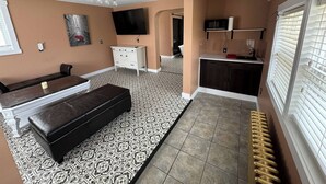 A living room with a sofa, ottoman, and a TV mounted on the wall. - The Red Farm Suite at The Red Farm (Howie Centre)