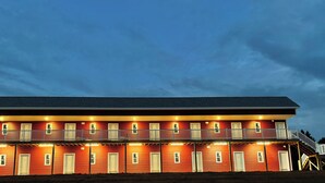 A two-story building with multiple windows and balconies, featuring a flat roof and a covered front porch.
