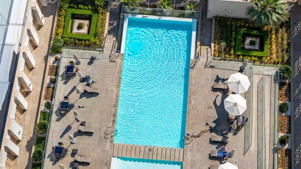 Vista aérea de uma piscina retangular com um deck ladrilhado ao redor, equipada com espreguiçadeiras e guarda-sóis.