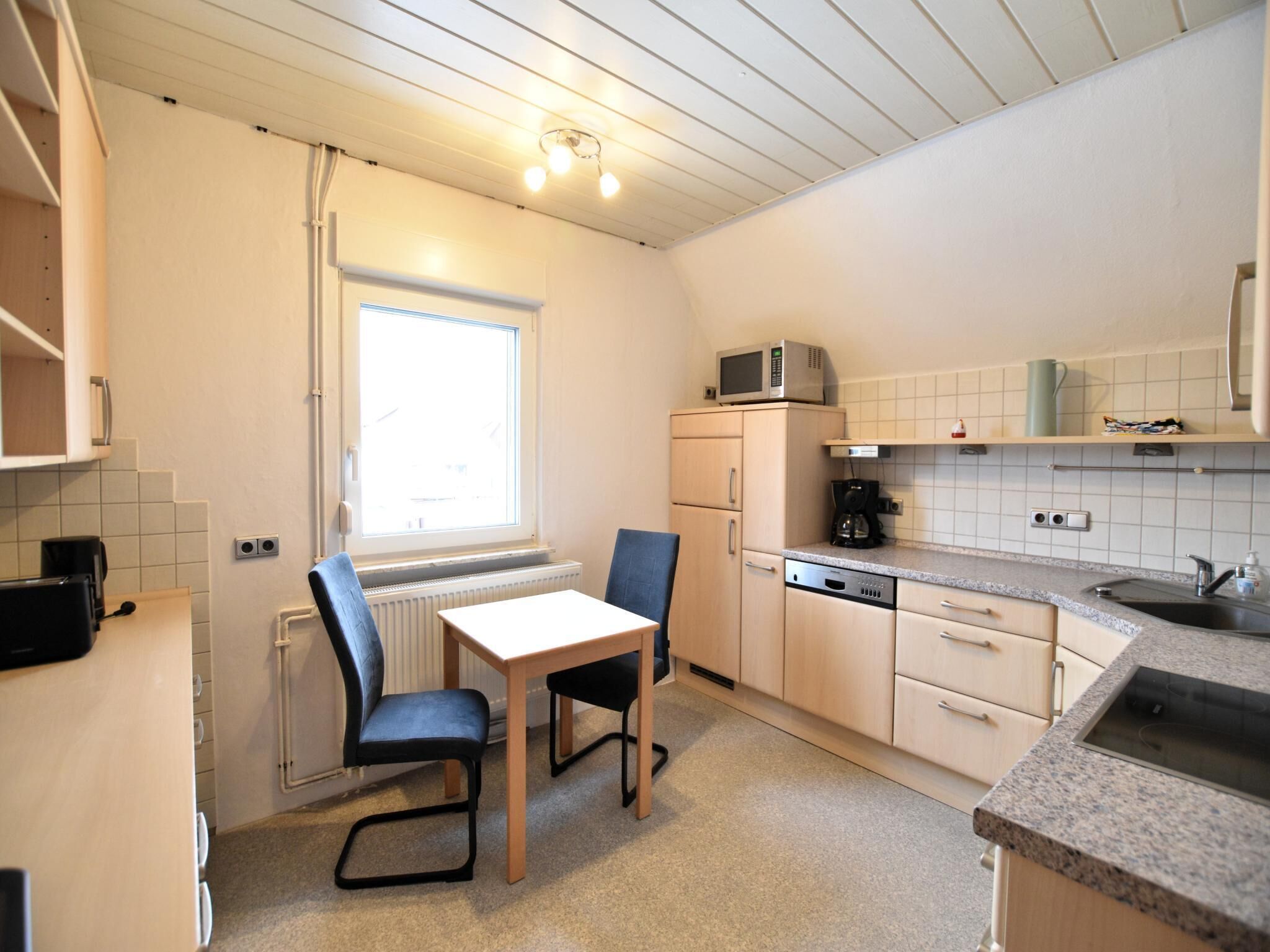 Een kleine keuken met een eettafel, stoelen, een magnetron, een koffiezetapparaat en een spoelbak.