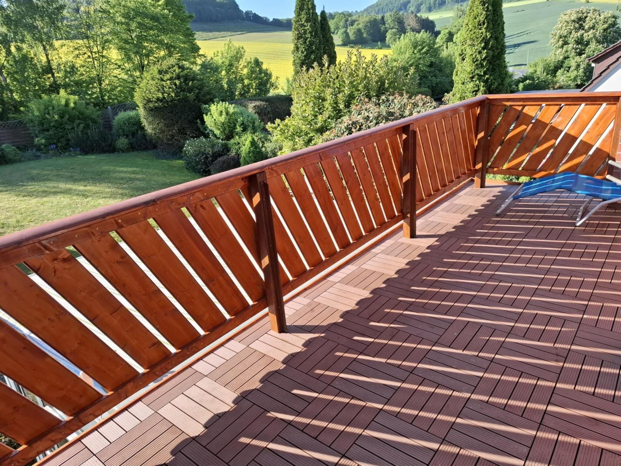 Une terrasse en bois avec une balustrade donnant sur un paysage verdoyant.