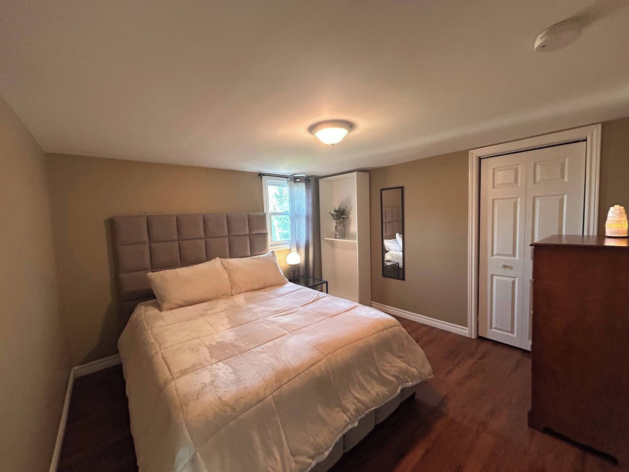 A bedroom with a large bed, a dresser, a mirror, and a door.
