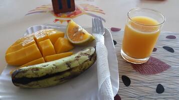 Ein Teller mit Mango-Scheiben, einer Banane und einem Glas Orangensaft auf einem Tisch mit gemustertem Tischläufer.