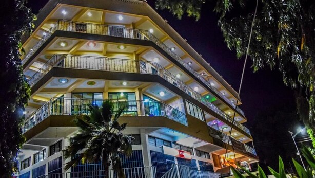 A multi-story hotel with balconies and a palm tree in the foreground. - The Joy Hotel Voi (Voi)