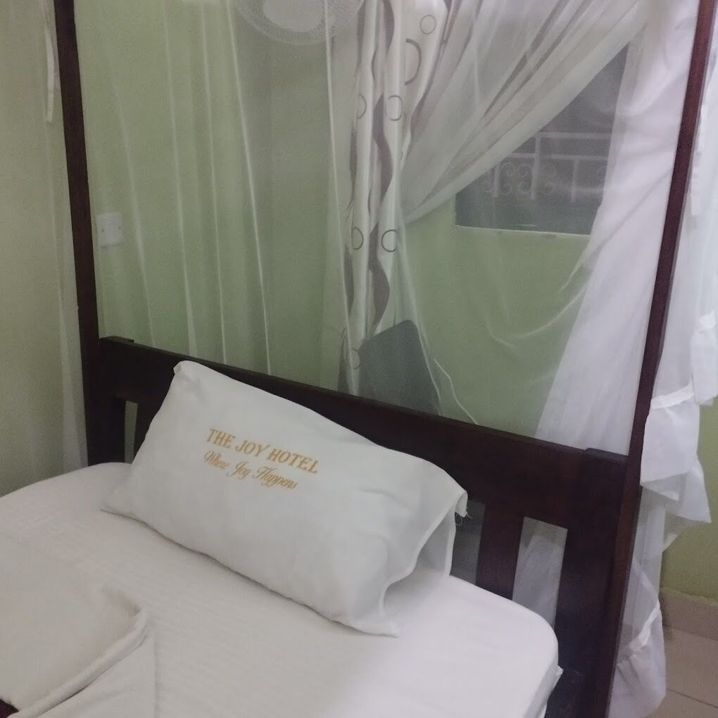 A hotel room with a bed, a pillow with the hotel name, and a window with curtains.