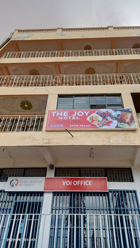 A hotel with a sign for "The Joy Hotel" advertising accommodation, restaurant, and parking.