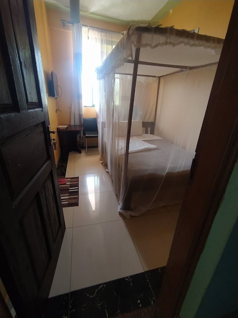 A room with a bed, a desk, and a chair. There is a window with curtains and a door.