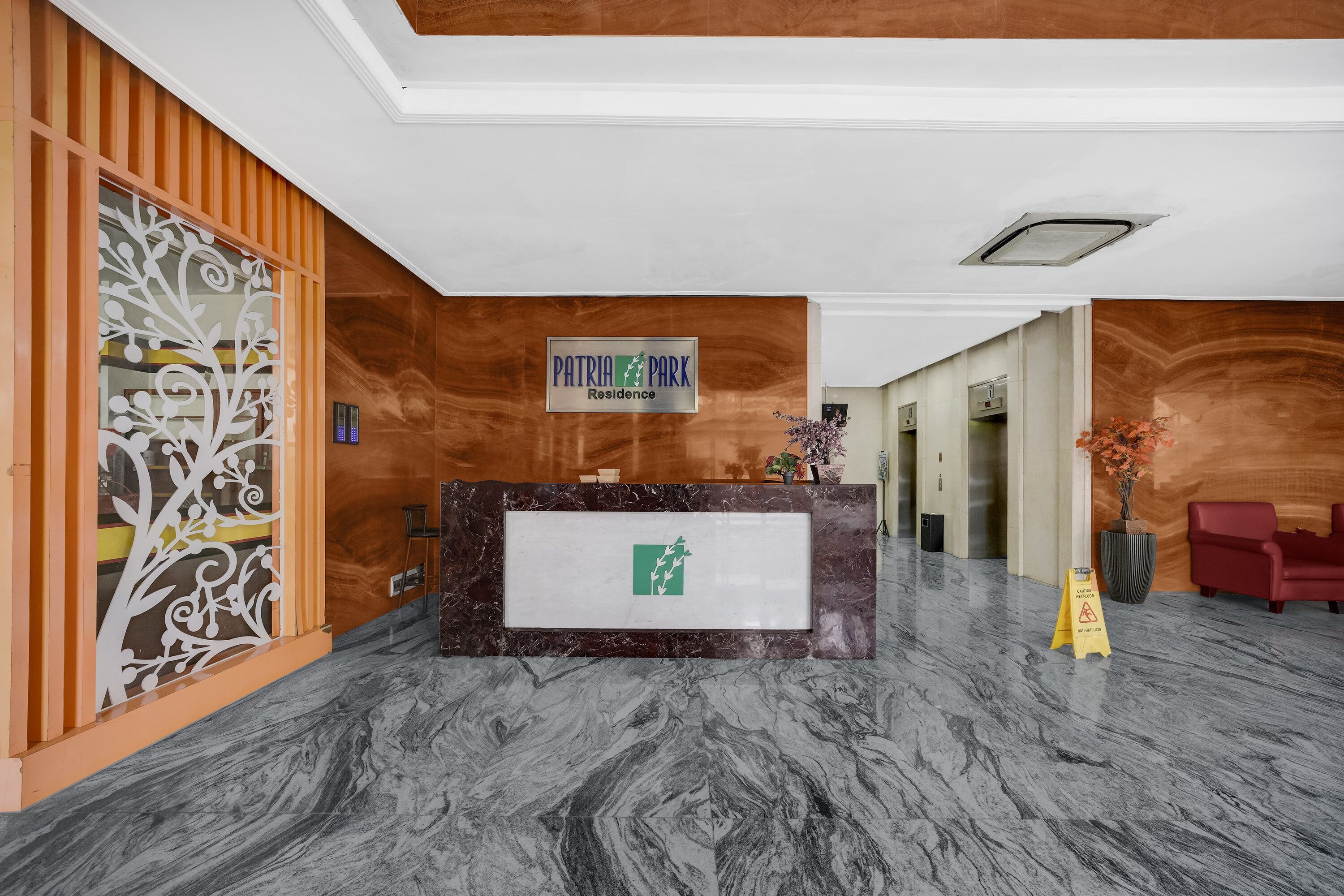 A reception area with a marble floor, a reception desk, a sign reading "Patria Park Residence," and a decorative glass partition.