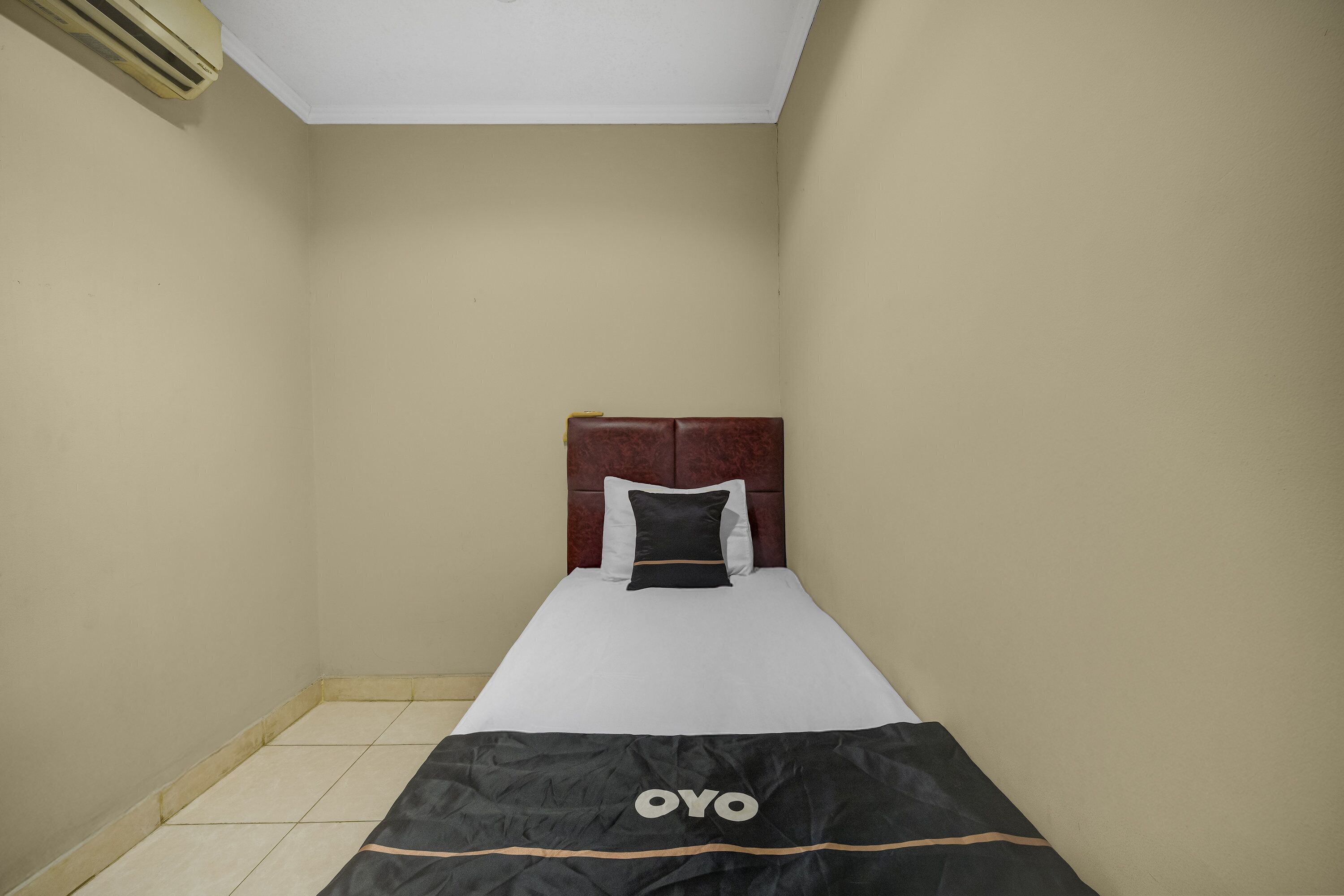 A small, single-bed room with a wooden headboard, a white mattress, and a black blanket with "OYO" branding.