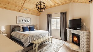 Une chambre à coucher comprenant un lit, des tables de chevet, un banc, une cheminée et un téléviseur.