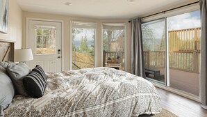 Une chambre avec un grand lit, une porte donnant sur un balcon et une vue sur une terrasse en bois.