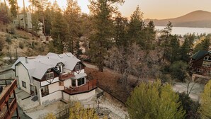 Une maison avec des fondations en pierre, une terrasse en bois et une vue sur un lac et des montagnes.