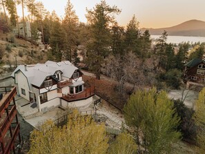 A house with a stone foundation, a wooden deck, and a view of a lake and mountains. - Elevated Escape | Bocce, Frisbee Glf, Walk to Town (Big Bear Lake)