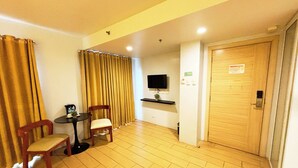 A hotel room with a wooden floor, a TV mounted on the wall, a door with a sign, and two chairs near a small table. - Foura Suites Makati (Makati)